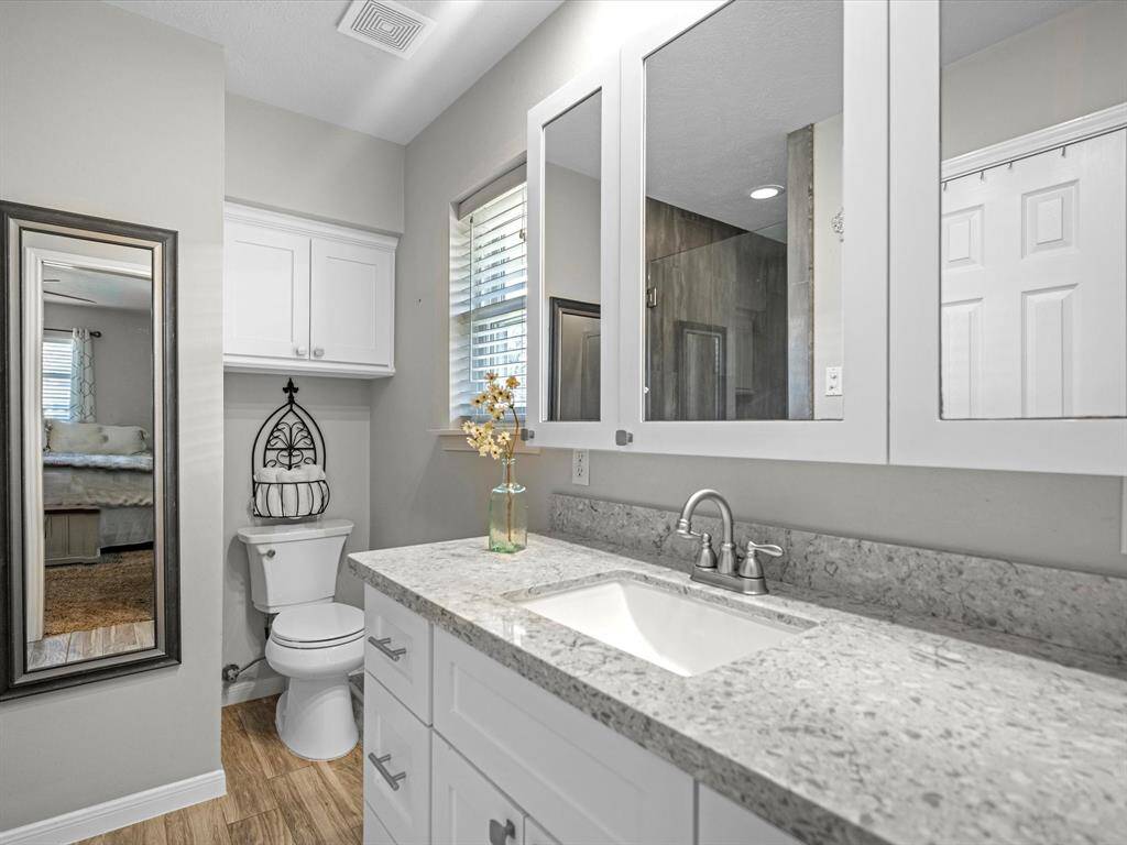 This secondary bathroom features a modern design with a granite countertop and white cabinetry.