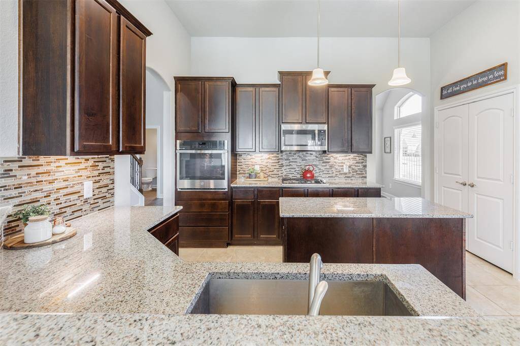 The spacious gourmet kitchen features a granite island & counters, gorgeous rich cabinetry, modern backsplash, gas cooktop & stainless steel appliances!