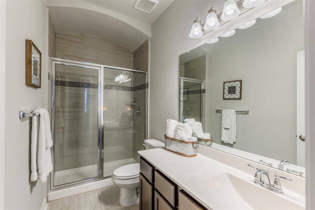 The secondary full bath provides a vanity counter, accent lighting and enclosed shower with tile surround.