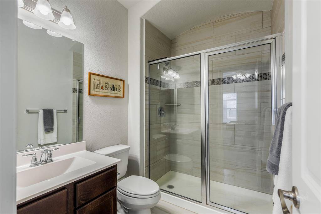 The secondary full bath provides a vanity counter, accent lighting and enclosed shower with tile surround.