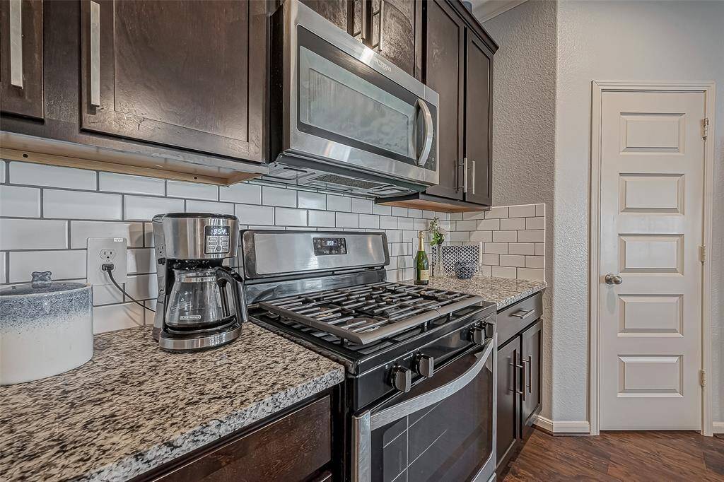 This kitchen features modern stainless steel appliances, granite countertops, and dark cabinetry. The white subway tile backsplash adds a clean, contemporary touch, while the laminate wood-like flooring enhances warmth and elegance.