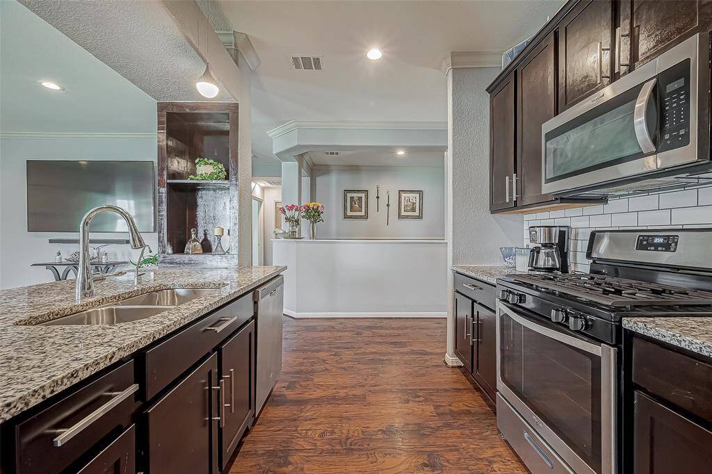 This kitchen features modern dark wood cabinets, stainless steel appliances, and granite countertops. The open layout flows into a dining area, with laminate wood-like floors adding warmth. Ample natural light and elegant finishes create a welcoming space.