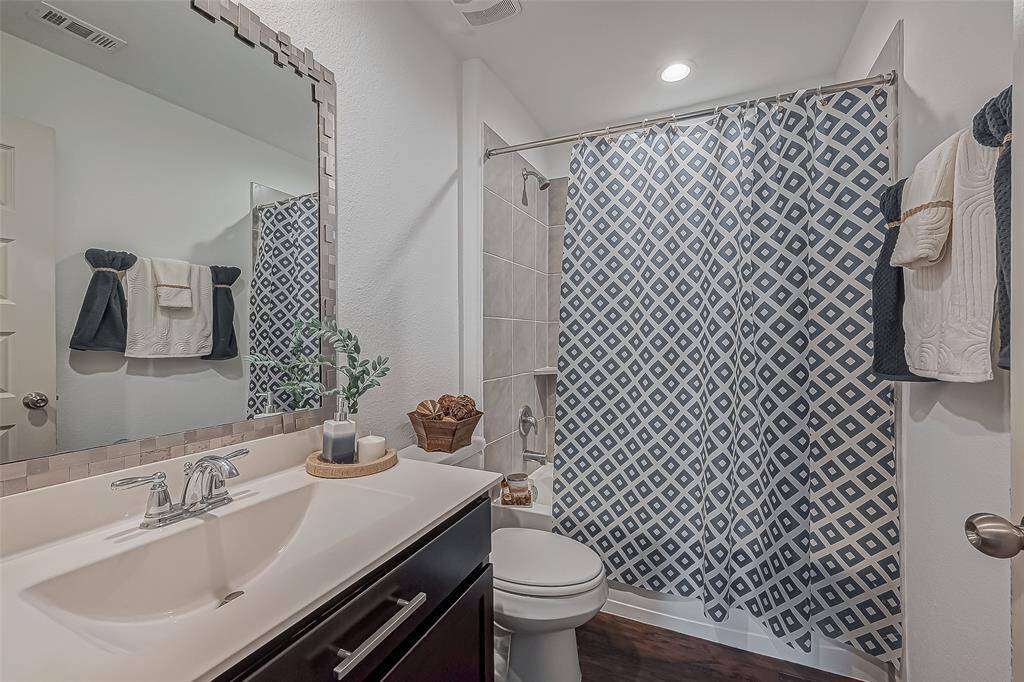 This bathroom features a modern design with a stylish vanity, a large framed mirror, and a shower-tub combo with a patterned curtain. The space is accented with neutral tones and thoughtful decor, creating a clean and inviting atmosphere.