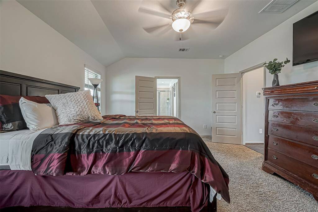 Spacious bedroom with plush carpeting, featuring a ceiling fan for comfort.The room leads to an ensuite bathroom through an open door, enhancing convenience and privacy.