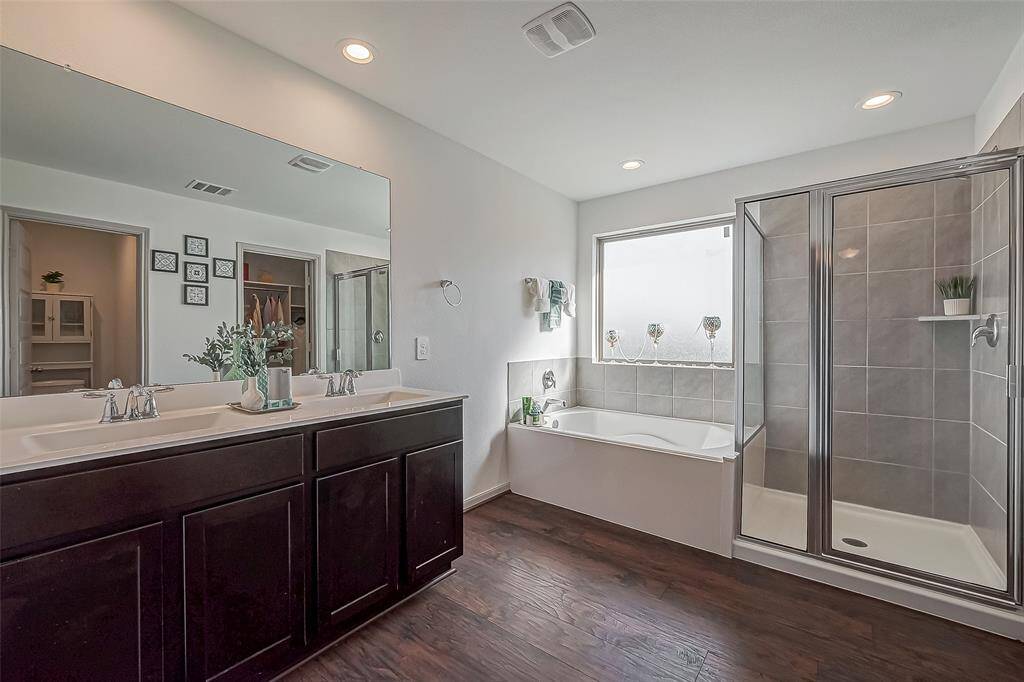 This modern bathroom features a double vanity with dark wood cabinets, a spacious glass-enclosed shower, and a separate bathtub. The room is well-lit with recessed lighting, and a large window provides natural light.