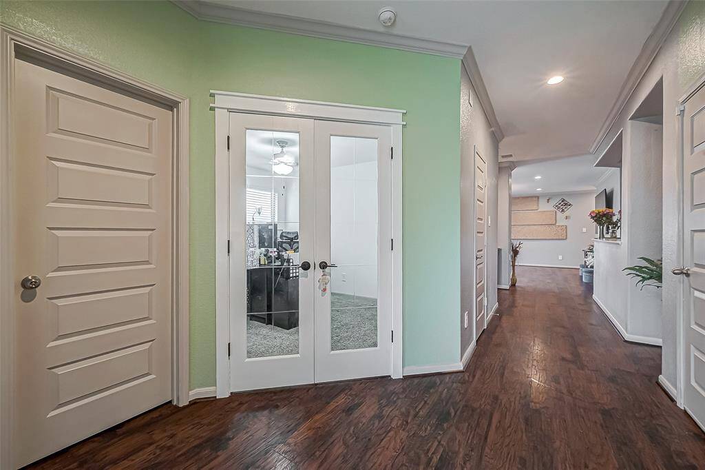 This photo showcases a welcoming hallway with laminate wood-like floors and soft green walls, leading to a living area. French doors open into a bright room, ideal for an office. The space is well-lit with recessed lighting, creating a warm ambiance.