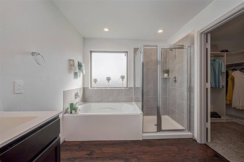 This bathroom features a sleek design with a modern bathtub, separate glass-enclosed shower, and a walk-in closet. It has stylish tile work, recessed lighting, and laminate wood-like flooring, offering a cozy, functional space.