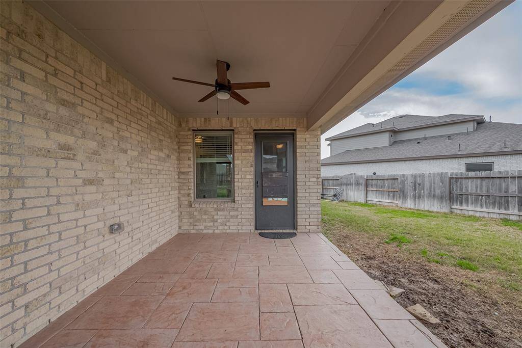 This photo showcases a covered patio with a ceiling fan, featuring brick walls and tiled flooring. It opens to a fenced backyard, providing a cozy outdoor space for relaxation or entertaining. Notice the storm doors on the front and back door.