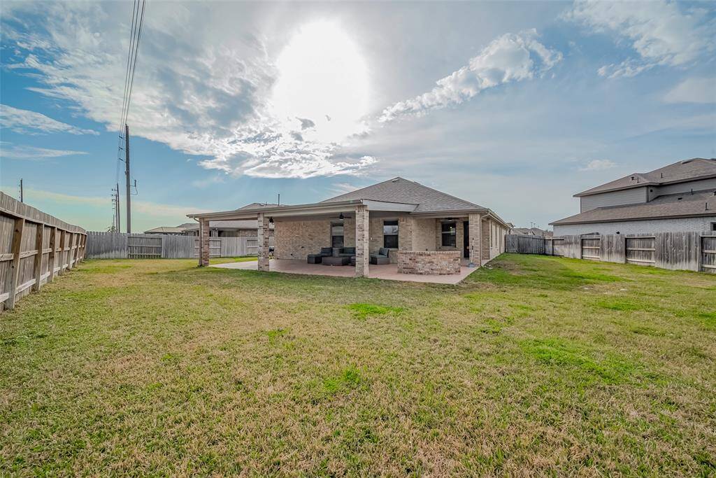 A spacious backyard with a wooden fence that surrounds a brick house featuring an over-sized covered patio, perfect for outdoor relaxation. The area is open and  ideal for gardening or play.