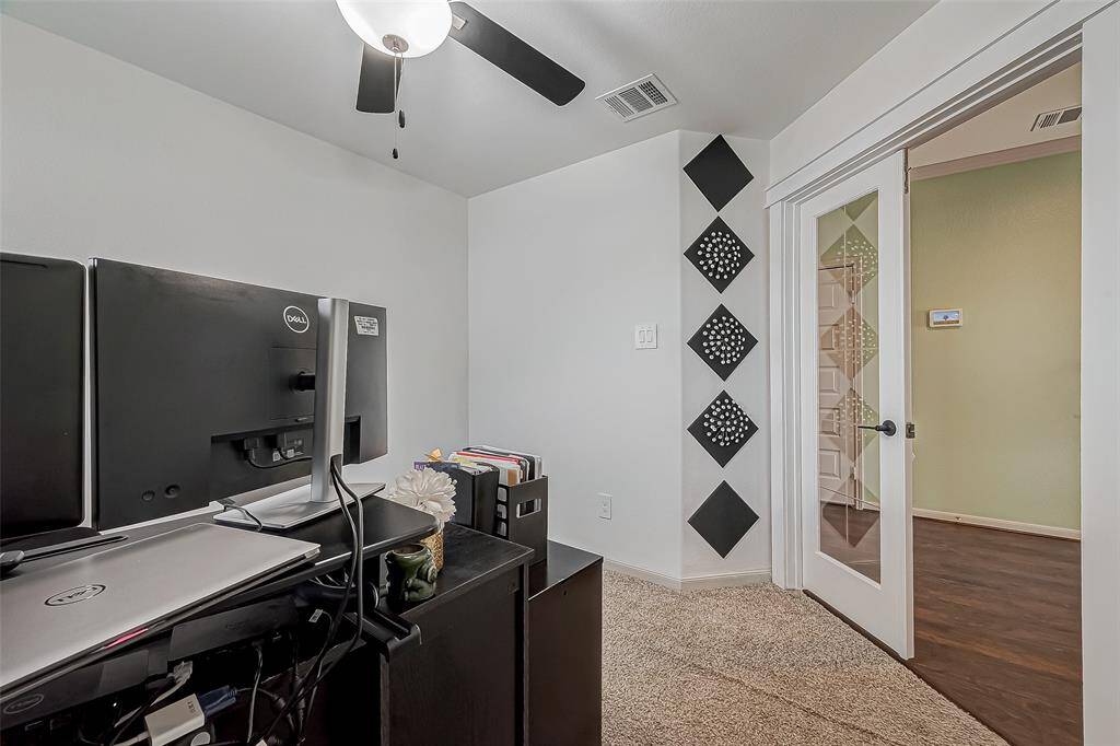 This photo shows a small home office with a modern design. There's a ceiling fan for ventilation and glass panel doors, providing a sense of openness.