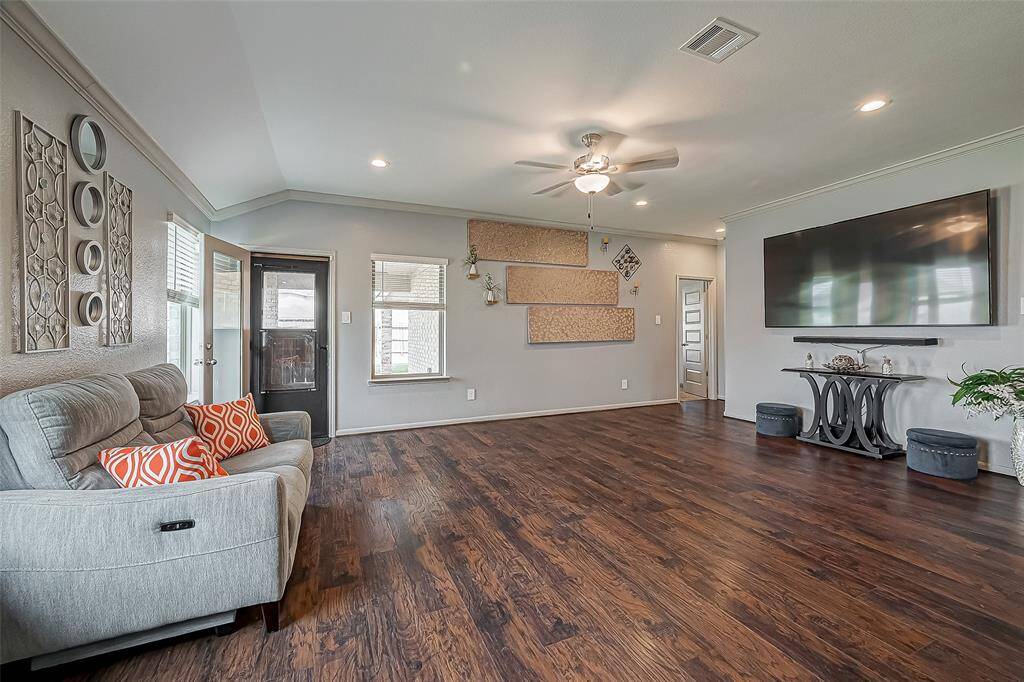 This spacious living room features laminate wood-like floors, a ceiling fan, and recessed lighting. This pretty room has ample natural light from multiple windows and a glass door leading to an outdoor covered porch.