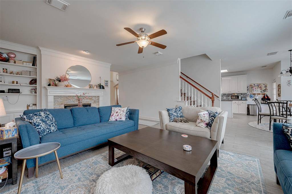 This inviting living room features a cozy fireplace, built-in shelves, and a ceiling fan. It flows seamlessly into the kitchen and dining area, with a staircase leading to the upper level. The space is bright and open, with modern furnishings and neutral tones.