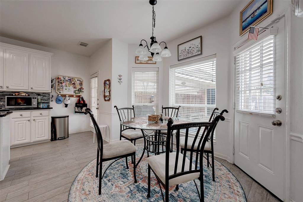 This photo showcases a bright dining area with large windows, a round rug, and a glass-top table surrounded by iron chairs. The adjacent kitchen features white cabinetry and modern appliances, creating a cozy and inviting space for meals.