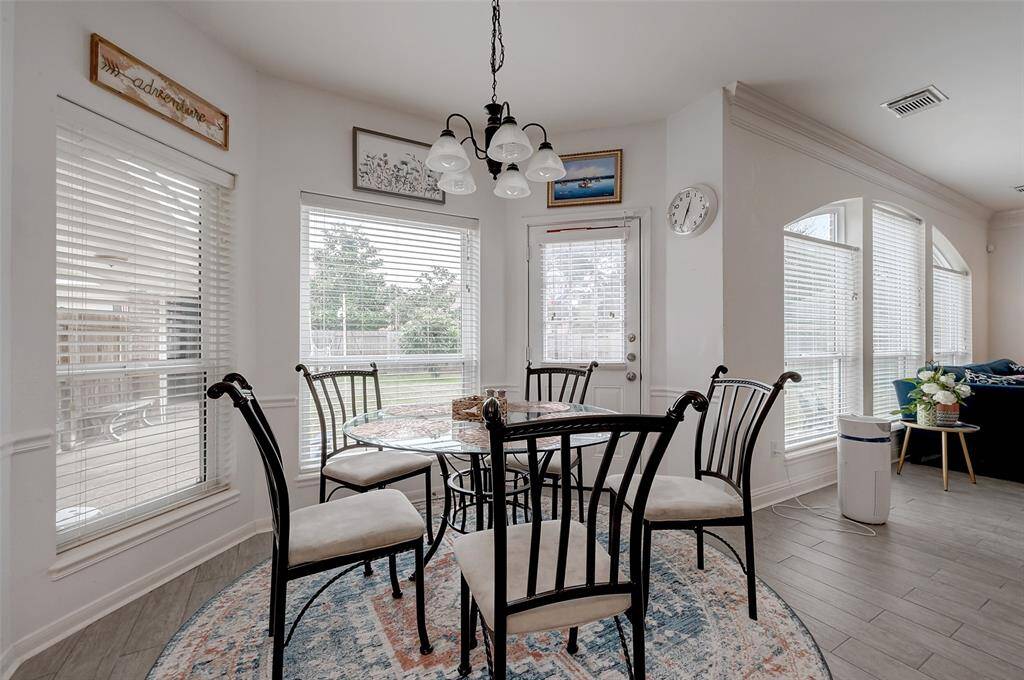 This bright dining area features a round table with seating for six, set on a patterned rug. Large windows provide ample natural light and offer views of the backyard. The space is accented with a hanging light fixture and tasteful wall decor.