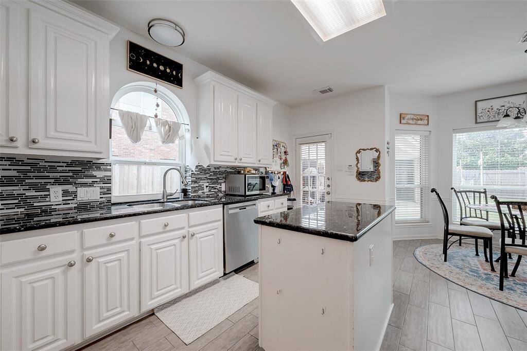 This bright, modern kitchen features white cabinetry, sleek black countertops, and a stylish tile backsplash. Ample natural light streams through the arched window, and there's an adjoining dining area with large windows overlooking the backyard, perfect for family meals.
