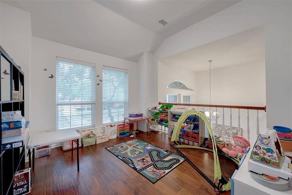 This photo showcases a bright, versatile playroom or study area with hardwood floors, large windows providing natural light, and ample storage space. It's located on an upper level, overlooking a staircase, ideal for a family-friendly environment.