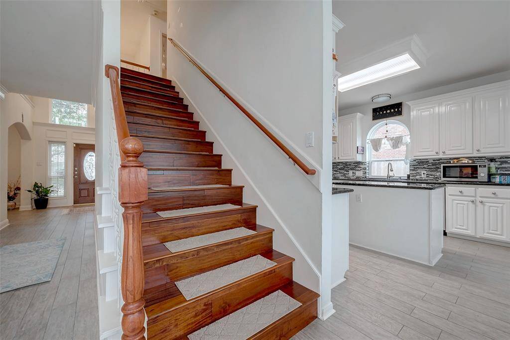 This photo showcases a bright and inviting entryway with a wooden staircase leading to the upper floor. To the right, there's a modern kitchen featuring white cabinetry and a stylish backsplash. The space is open and filled with natural light, creating a welcoming atmosphere.