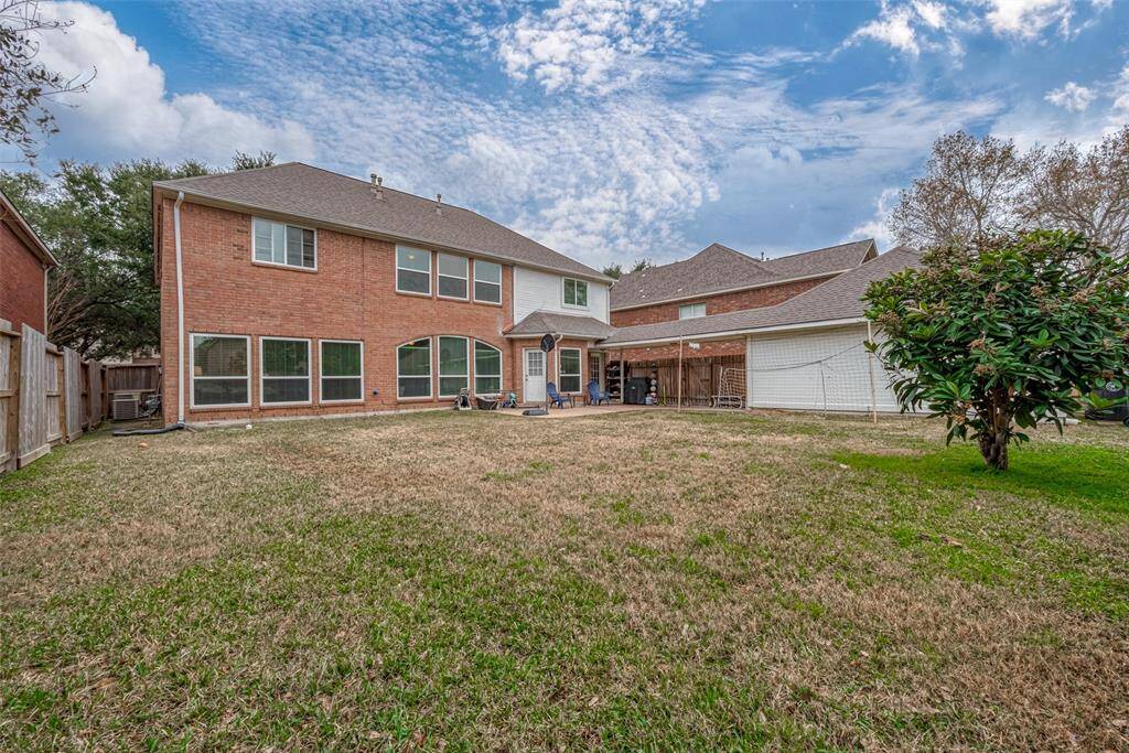 This photo shows a spacious two-story brick home with a large backyard. The yard is mostly grass with a few trees and a covered patio area. The home has multiple windows, offering plenty of natural light, and the backyard is enclosed with a wooden fence, providing privacy.