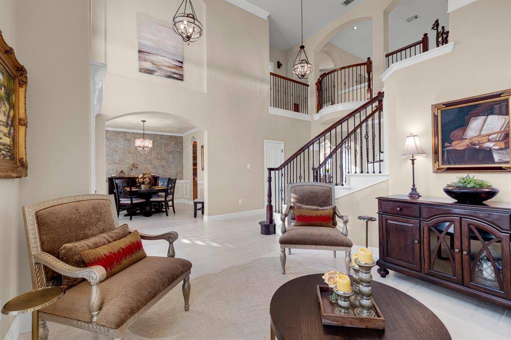Elegant, open-concept living space featuring high ceilings, a grand staircase with iron balusters, and an arched entryway leading to a formal dining area. The room is well-lit with natural light and stylish pendant lighting.
