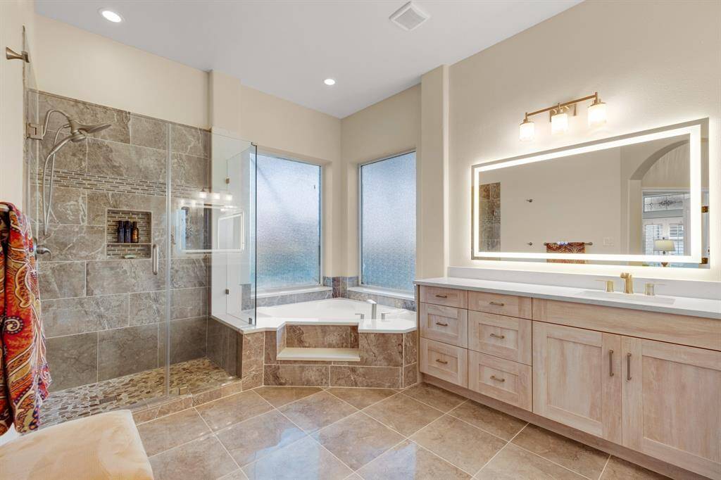 A spacious, modern bathroom featuring a large walk-in shower with glass enclosure, a built-in bathtub, dual-sink vanity with ample storage, and a frosted window providing natural light while ensuring privacy.  2'x4' porcelain tile.