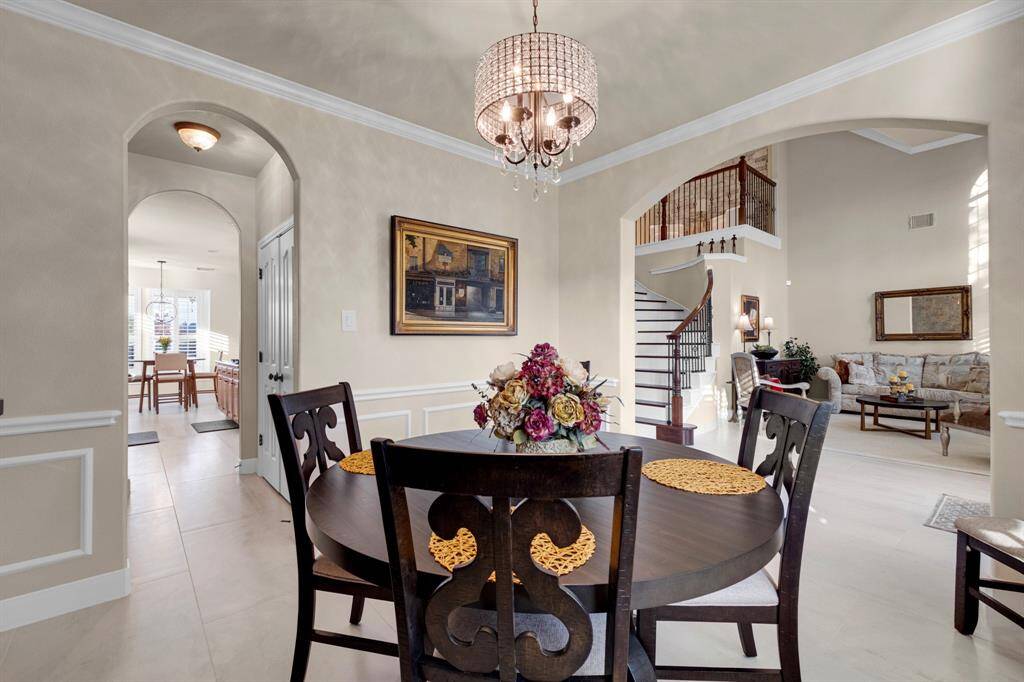 A spacious, open-concept home featuring an elegant dining area with a modern chandelier, leading into a cozy living room with high ceilings and a grand staircase. The interior is well-lit, with a neutral color palette that provides a warm and inviting atmosphere.
