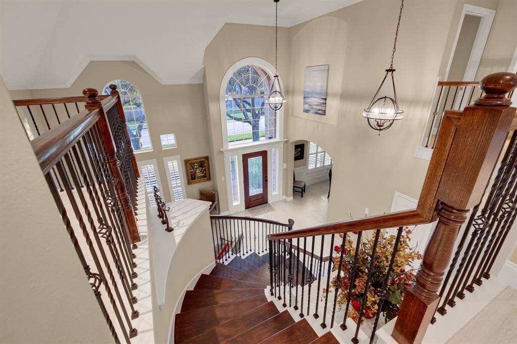 A spacious two-story entryway with an elegant staircase, high ceilings, arched windows, and stylish pendant lighting, creating an open and inviting atmosphere for a luxurious home.