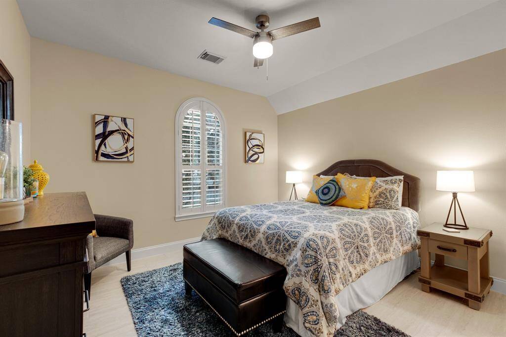 A cozy, well-lit bedroom. ceiling fan, elegant arched window with shutters, and a comfortable seating area.