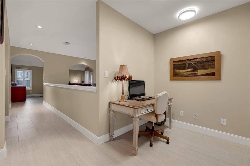 A well-lit hallway space with an office nook, featuring 1'x2' porcelain flooring, neutral wall colors, and arched pass-throughs to adjacent rooms, providing an open and airy feel.