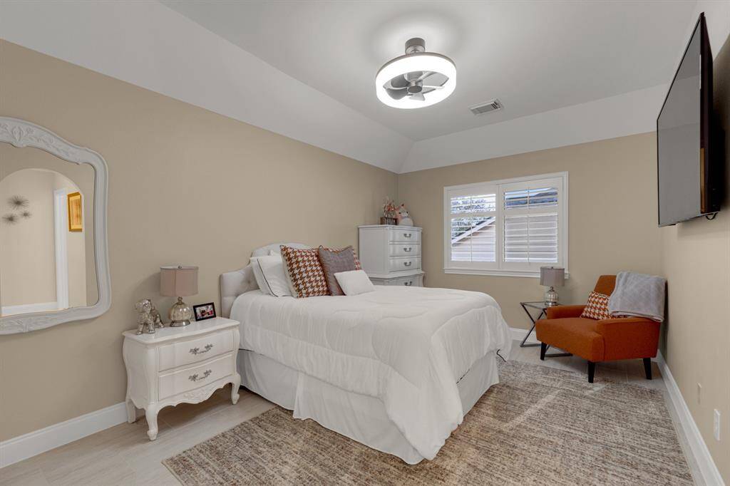 A cozy, well-lit bedroom featuring a neutral color palette,. A large window allows for ample natural light, and the room includes modern lighting fixture creating a welcoming and serene space.