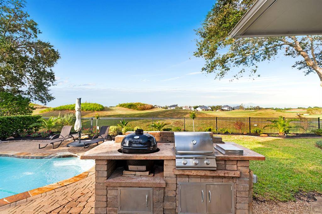 A spacious backyard with a built-in barbecue grill, a swimming pool, and a relaxing view of a golf course beyond a wrought-iron fence, ideal for outdoor entertainment and leisure.