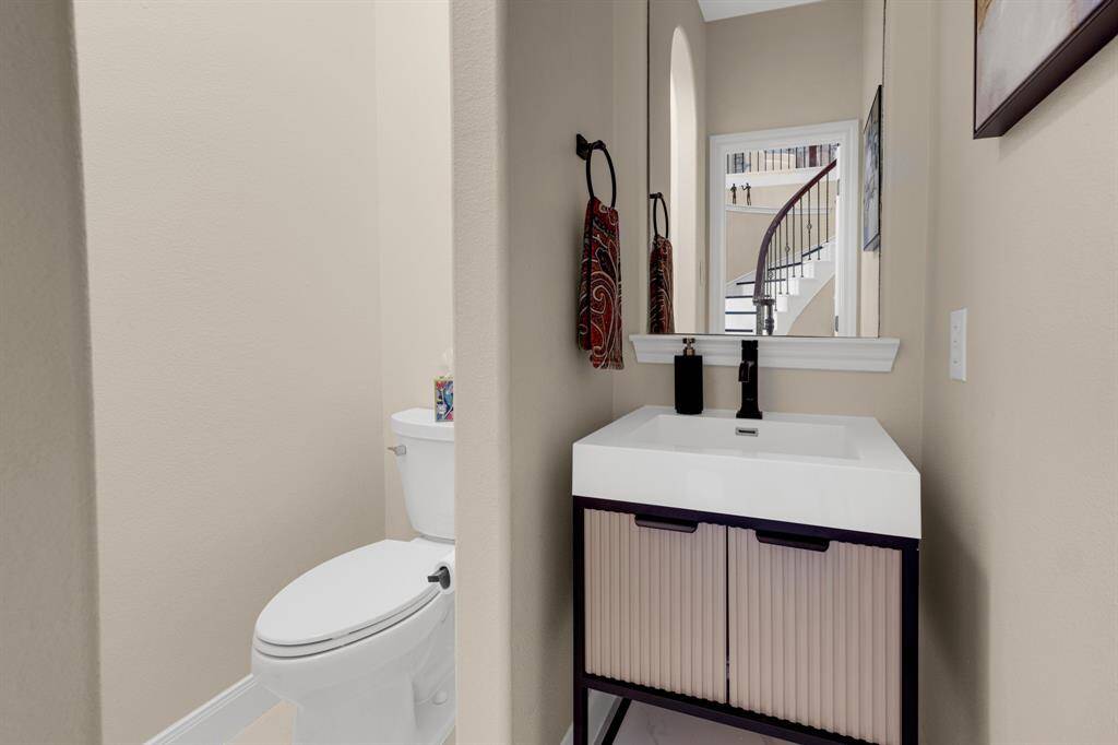 Compact and modern half-bathroom with a sleek toilet and a vanity with a vessel sink. The space is efficiently designed and features neutral colors with a view of a staircase in the background, suggesting a multi-level home layout.