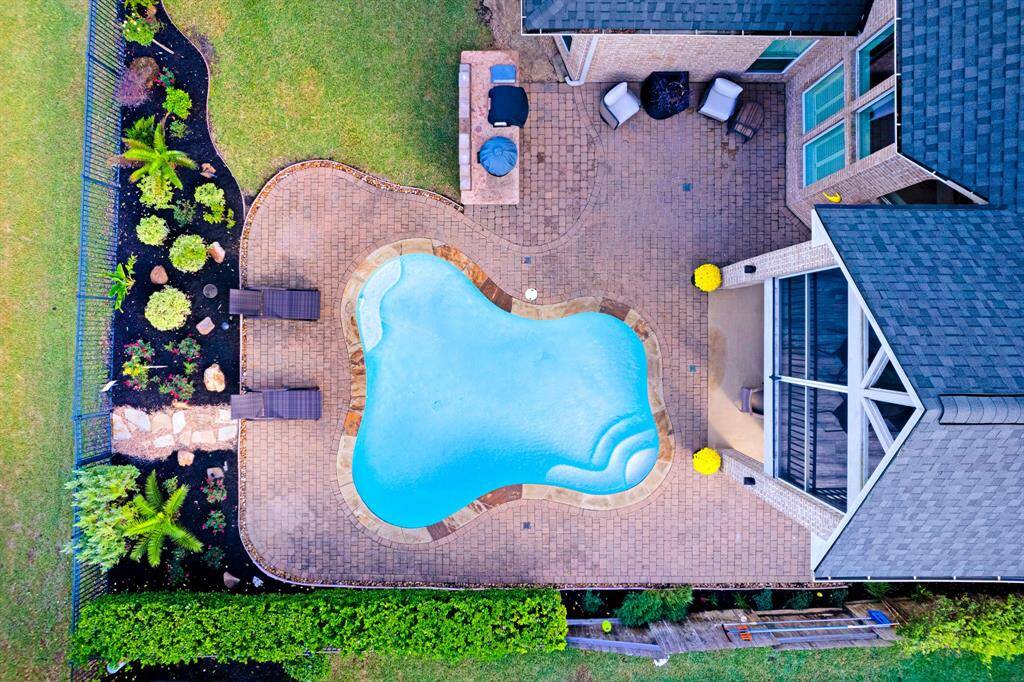 The aerial view showcases a beautiful backyard with an inviting kidney-shaped pool, surrounded by a well-maintained patio and vibrant garden beds, complementing a charming home with a striking roof design. NEW ROOF 2024