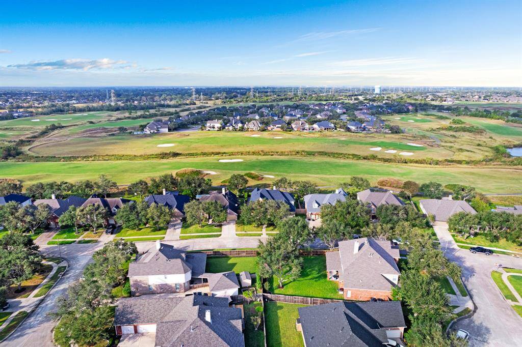 A residential community with spacious single-family homes along well-maintained streets, adjacent to a lush golf course with expansive greens and water features, offering a serene and picturesque living environment.