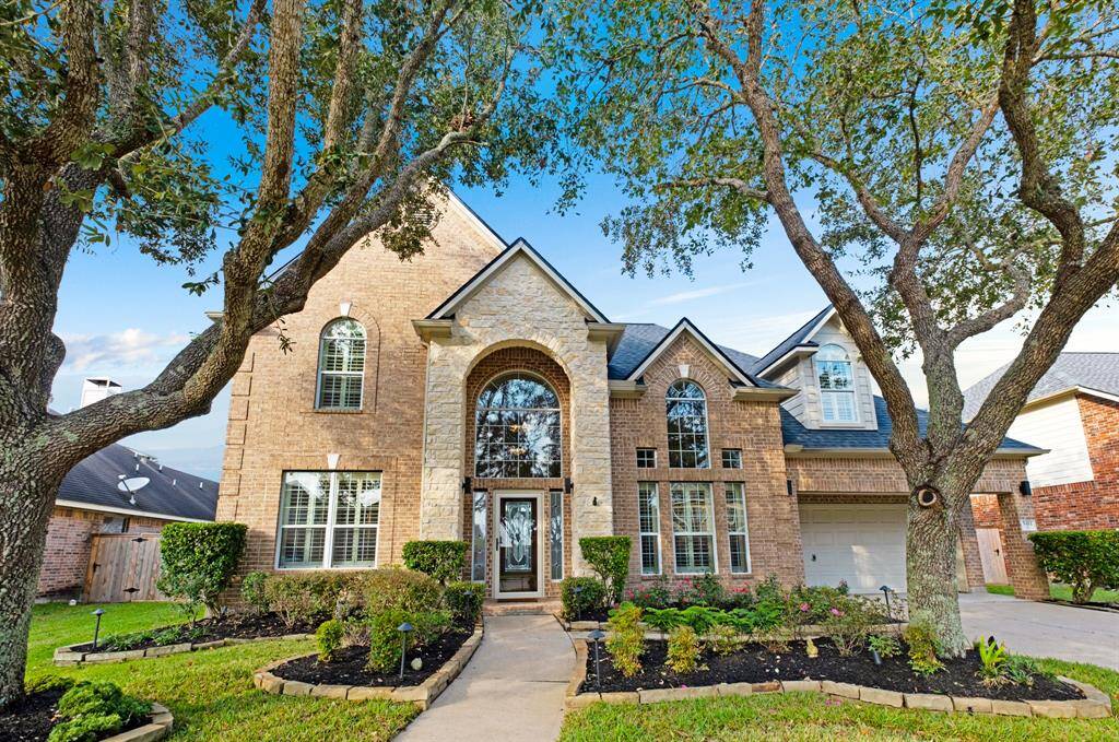 A spacious two-story brick home featuring a tall entryway, large windows, a three-car tandem garage.