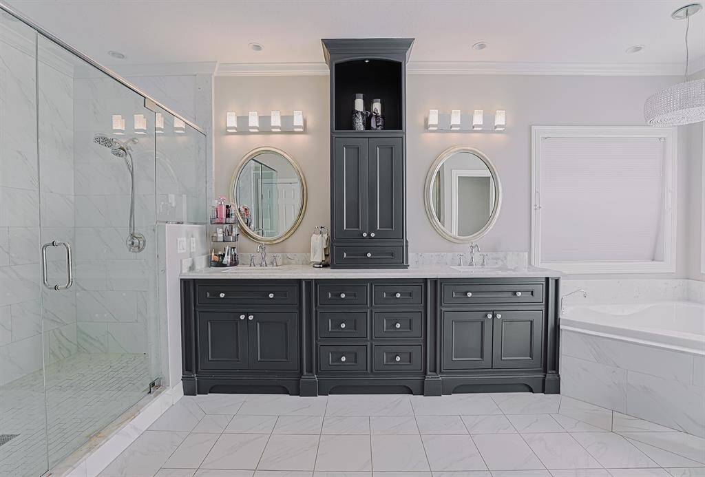A luxurious and modern bathroom featuring a spacious double vanity with granite countertops, a large frameless glass shower, and elegant lighting. The neutral color palette and sleek finishes create a spa-like ambiance.
