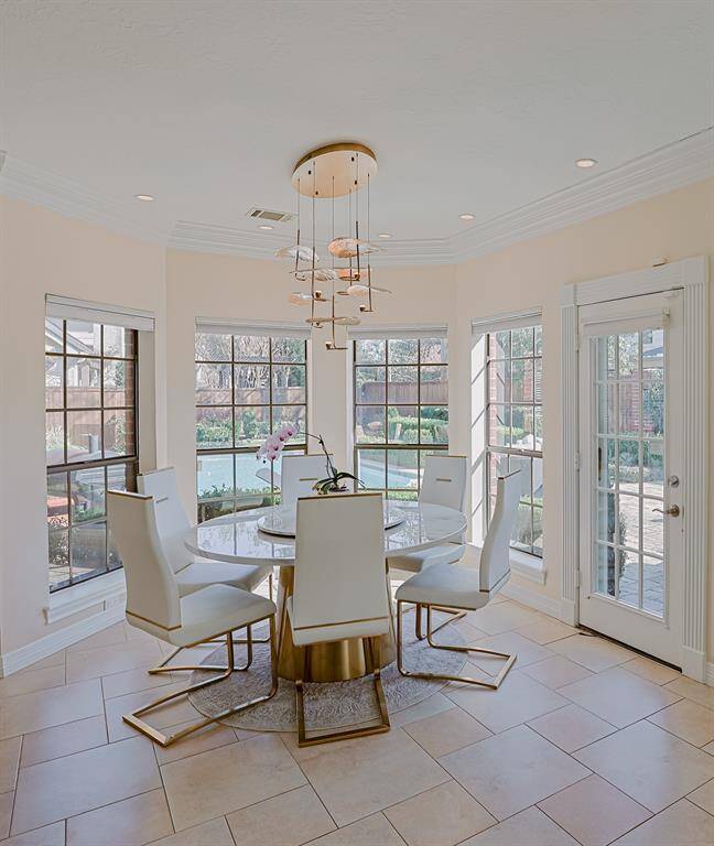 A bright and airy breakfast nook surrounded by large windows that offer a picturesque view of the backyard and pool. The modern chandelier and sleek furniture enhance the stylish, contemporary look.