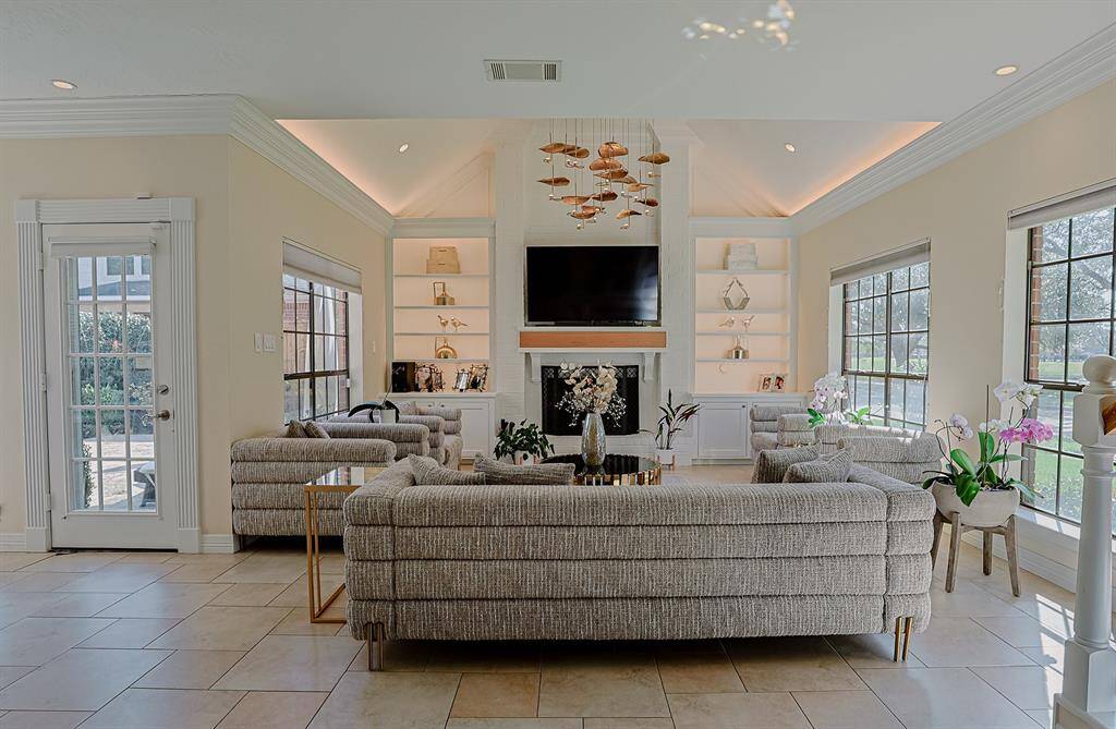 A beautifully designed living space with soaring ceilings, a modern fireplace, and built-in shelving. Expansive windows flood the room with natural light, while the elegant furnishings create a comfortable yet refined atmosphere.
