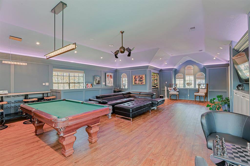 A sophisticated and spacious game room with a vaulted ceiling, wood flooring, and LED accent lighting. This space is perfect for entertaining, featuring a pool table, built-in bar, and comfortable seating.