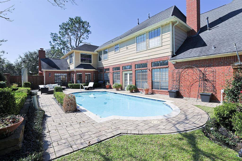 A private backyard retreat featuring a sparkling swimming pool surrounded by lush greenery and manicured hedges. The spacious stone-paved patio is perfect for lounging, and the backyard is equipped with a mosquito misting system for added comfort.