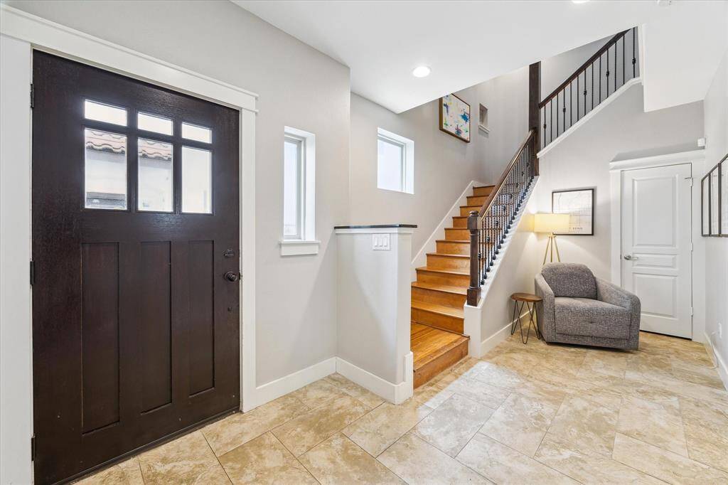 Modern home exterior featuring a stylish entrance with a dark wood door, stone accents, and a large two-car garage. The property has a landscaped front area and a clean, inviting driveway.