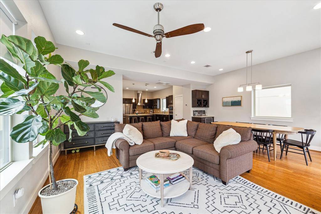 This bright, open-concept living and dining area features hardwood floors, modern lighting, and large windows. It includes access to a balcony through French doors, creating an inviting space for relaxation and entertaining.