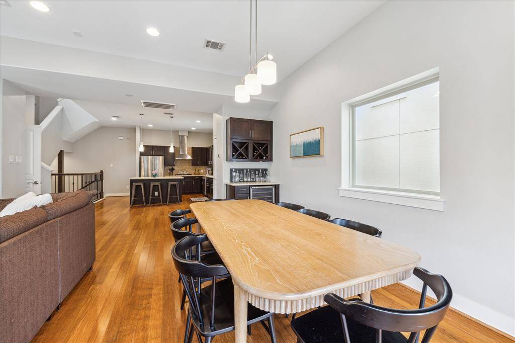 This photo showcases a modern open-concept living space with a spacious dining area and kitchen. The room features hardwood floors,  contemporary lighting, and a sleek kitchen with stainless steel appliances and a central island. The bright, neutral walls enhance the sense of space and light.