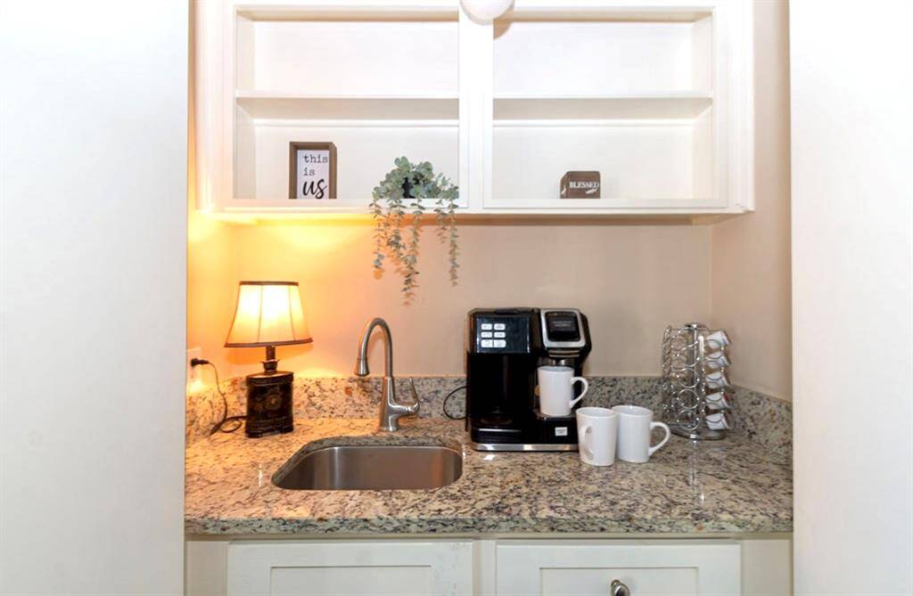 This cozy coffee nook with granite countertops, a small sink, and open shelving will showcase the connoisseur . Features a coffee maker, mugs, and decorative items, offering a charming spot for morning routines.
