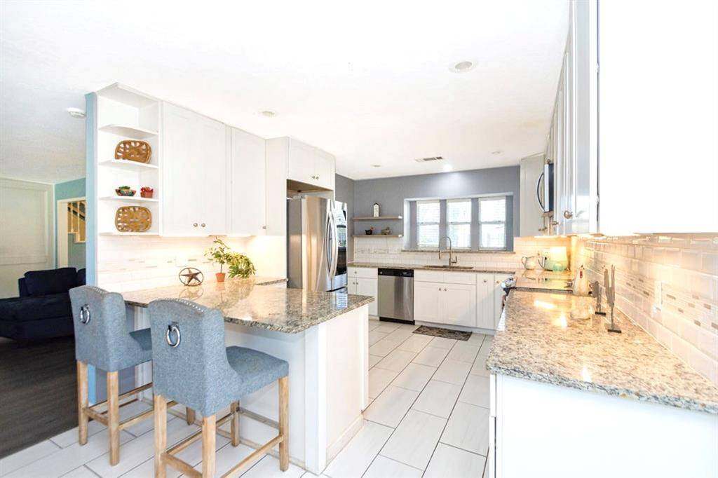 This bright kitchen features modern stainless steel appliances, granite countertops, and ample cabinetry. The open layout includes a breakfast bar with seating, and a large window over the kitchen sink provides plenty of natural light!