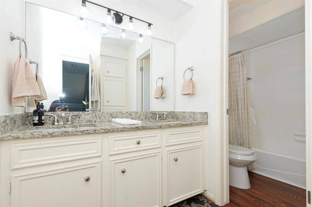 Secondary Full Bathroom has updated lighting, granite, dual undermount sinks, faucet, commode, wood laminate flooring, it also has a linen closet and clothes hamper, and the bathtub was just reglazed in 2024!