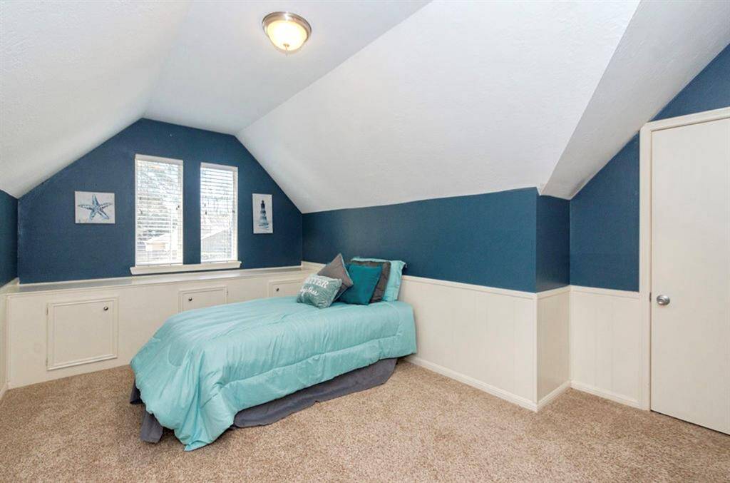 This cozy bedroom (Bedroom 3) features a sloped ceiling, soft carpet, and calming blue walls with white wainscoting. It also includes Low E Double Pane windows for natural light, and built-in storage cabinets.