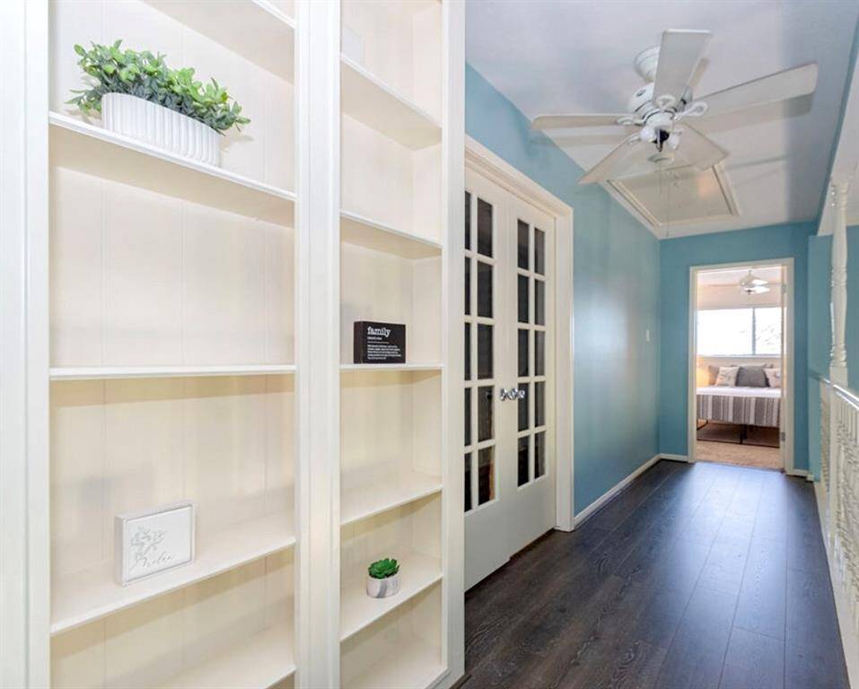 This hallway features elegant built-in shelves and stylish French doors, leading to a cozy bedroom. The space has a soothing blue wall color and 2024 LVP flooring, and a ceiling fan + light!