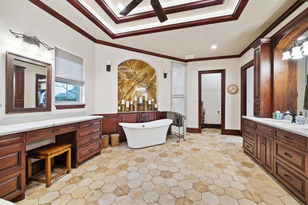 This spacious primary bathroom features a luxurious freestanding tub, and a walk-in shower with a programable temperature and shower head control  There are separate dual vanities with ample storage, and elegant tile flooring. The room is accented by rich wood cabinetry and a striking ceiling design, creating a warm and inviting atmosphere.