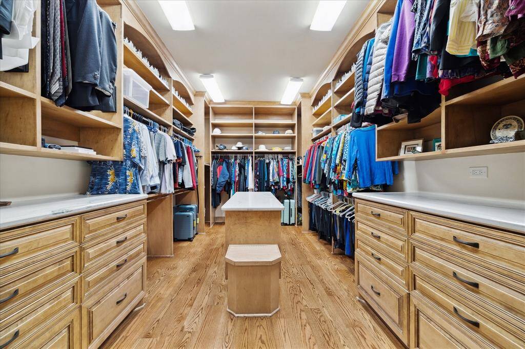 This view of the primary bedroom closet focuses on the myriad of custom built-in cabinetry, drawers, shelves and island.