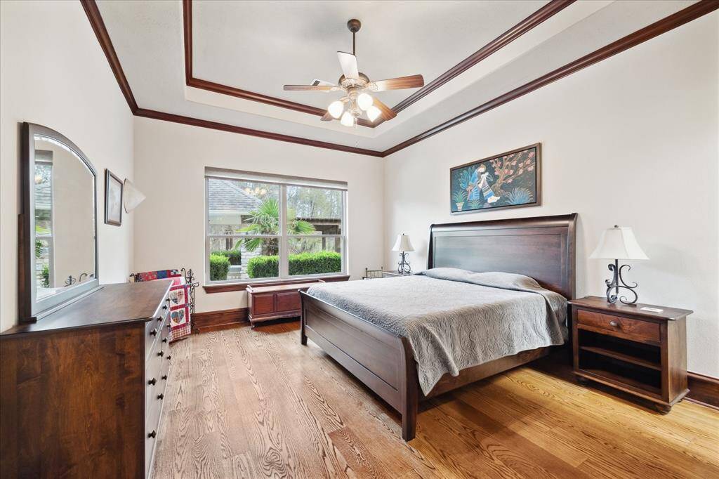 This spacious secondary bedroom on the first floor with an ensuite bathroom features hardwood floors, a large window with garden views, and elegant wood trim. It includes a ceiling fan, ample light, creating a cozy and inviting atmosphere.